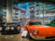 Large showroom with vintage restored cars in the foreground and restored motorbikes in background.